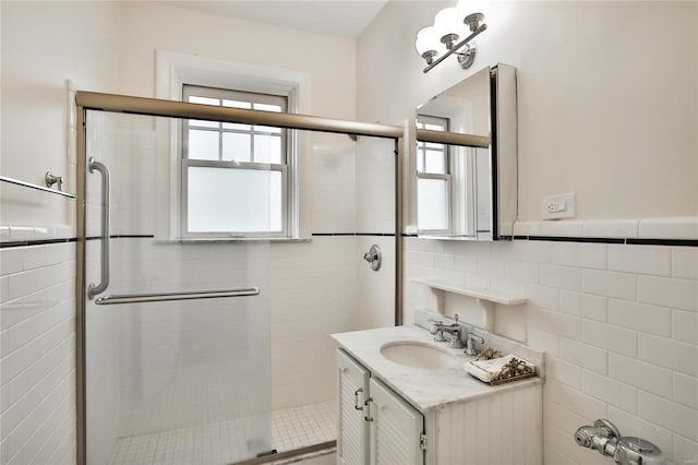 full bath featuring tile walls, a stall shower, vanity, and wainscoting