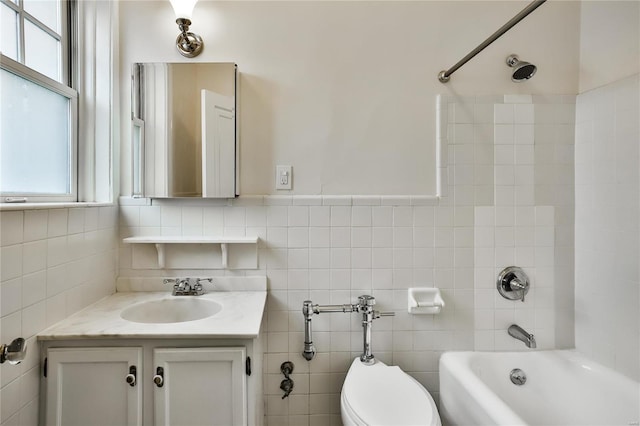 full bath with healthy amount of natural light, toilet, tub / shower combination, vanity, and tile walls