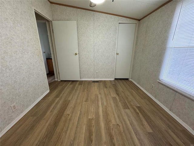 65 Bright St, Troy, MO 63379 - unfurnished bedroom featuring crown molding, wood finished floors, wallpapered walls, and vaulted ceiling