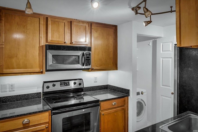 kitchen featuring appliances with stainless steel finishes, washer / clothes dryer, brown cabinetry, and dark stone counters