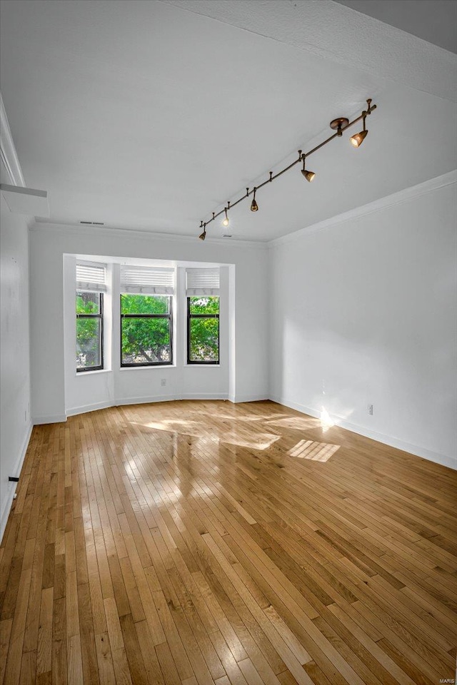 empty room featuring track lighting, light wood-type flooring, baseboards, and crown molding