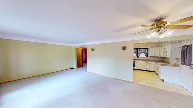 unfurnished living room featuring ceiling fan, ornamental molding, light colored carpet, a sink, and baseboards