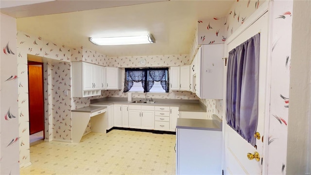 kitchen featuring a sink, light flooring, white cabinets, and wallpapered walls