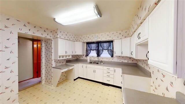 kitchen with wallpapered walls, light floors, white cabinetry, and a sink