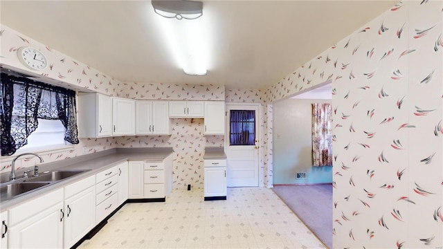 kitchen featuring a sink, light floors, wallpapered walls, and white cabinets