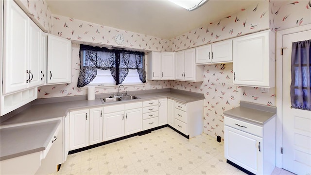 kitchen featuring a sink, wallpapered walls, white cabinetry, and light floors