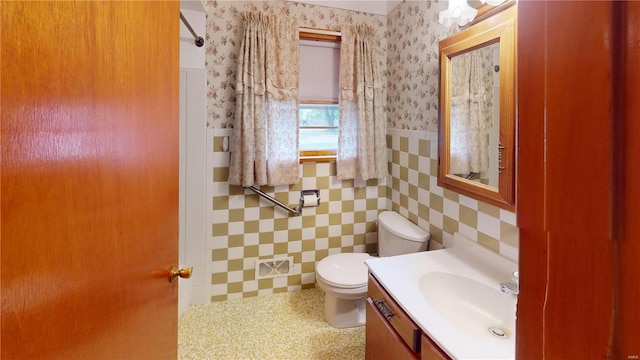 bathroom with tile walls, toilet, visible vents, vanity, and a wainscoted wall
