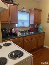 kitchen with white electric range, a sink, brown cabinetry, dark wood-type flooring, and dark countertops