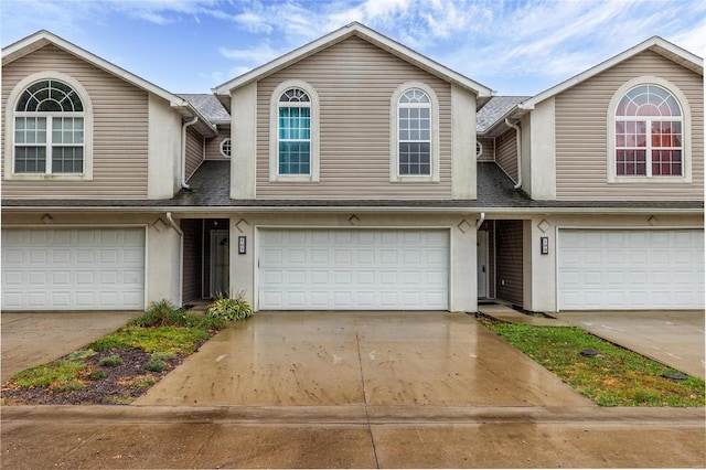 multi unit property with a garage, concrete driveway, stucco siding, and roof with shingles