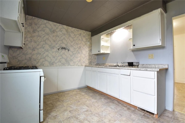 1103 S Madison St, Gillespie, IL 62033 - kitchen with white range with gas stovetop, a wainscoted wall, white cabinetry, wallpapered walls, and a sink