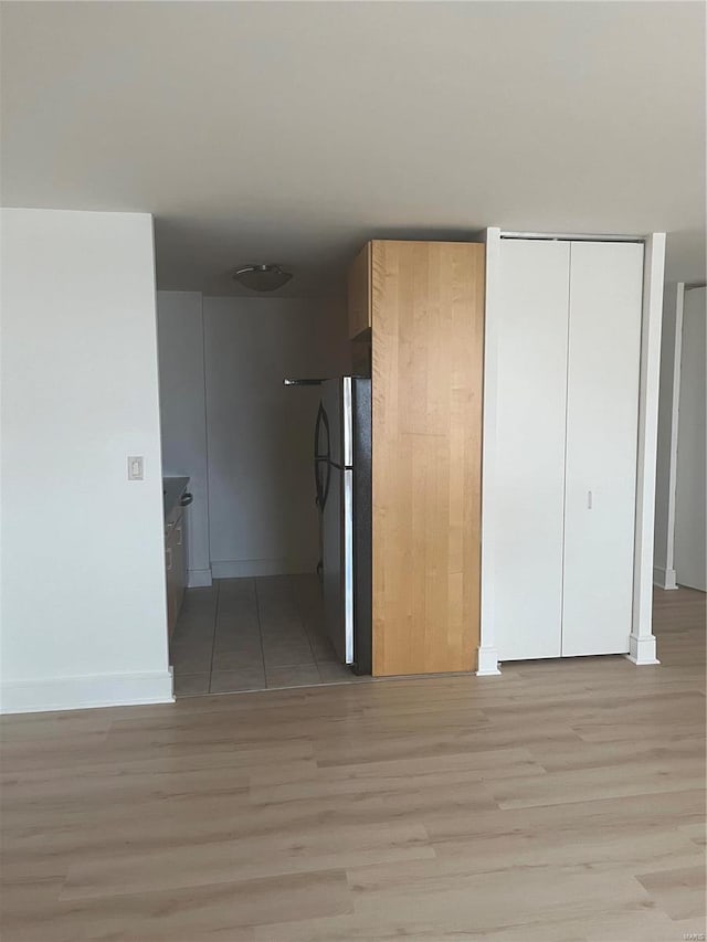 interior space featuring freestanding refrigerator, light wood finished floors, a closet, and baseboards
