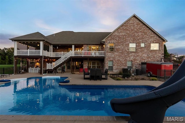 pool at dusk with a water slide, stairs, a patio, a wooden deck, and fence