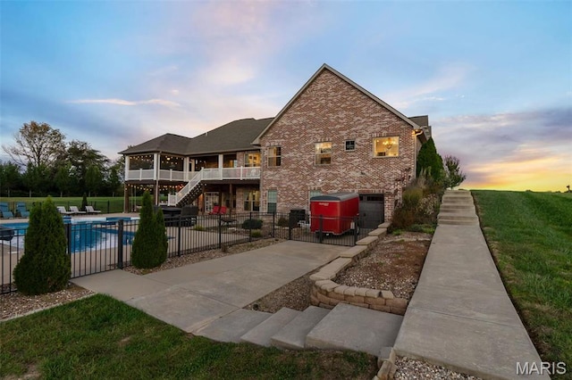 back of house at dusk featuring fence, stairway, and brick siding