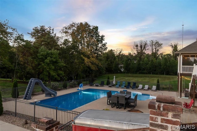 pool at dusk featuring a water slide and a patio