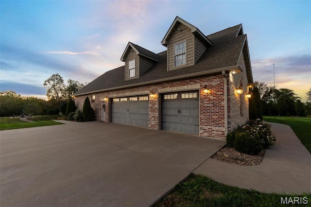 property exterior at dusk with brick siding, concrete driveway, an attached garage, and roof with shingles