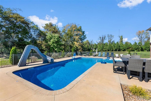 view of swimming pool featuring a water slide, fence, a patio, and view of wooded area