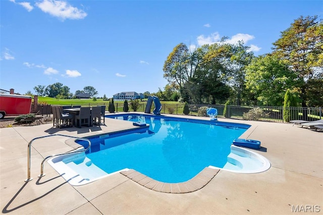 view of swimming pool featuring a patio area, fence, outdoor dining space, and a water slide
