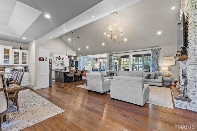 living area with high vaulted ceiling, a stone fireplace, a chandelier, dark wood-style floors, and recessed lighting