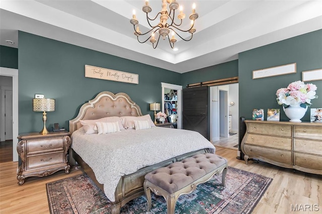 bedroom featuring a barn door, a chandelier, light wood-style flooring, and a tray ceiling