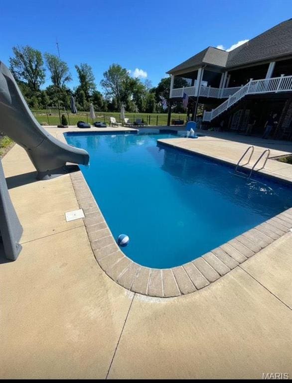 view of pool featuring a water slide, fence, a patio area, and stairway