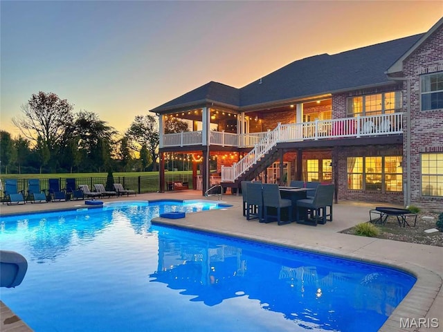 pool at dusk featuring stairway, a patio, and fence