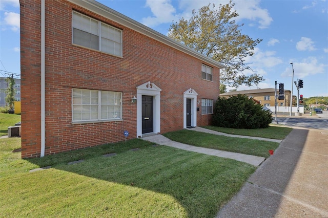view of front facade featuring a front yard, brick siding, and central air condition unit