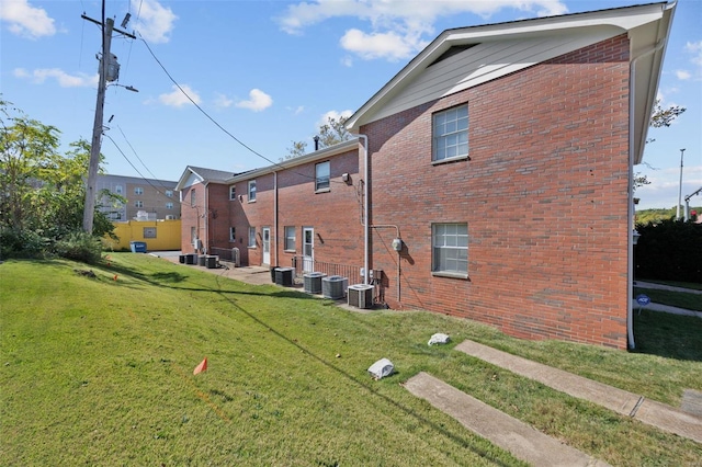 view of side of property with brick siding, a yard, and cooling unit