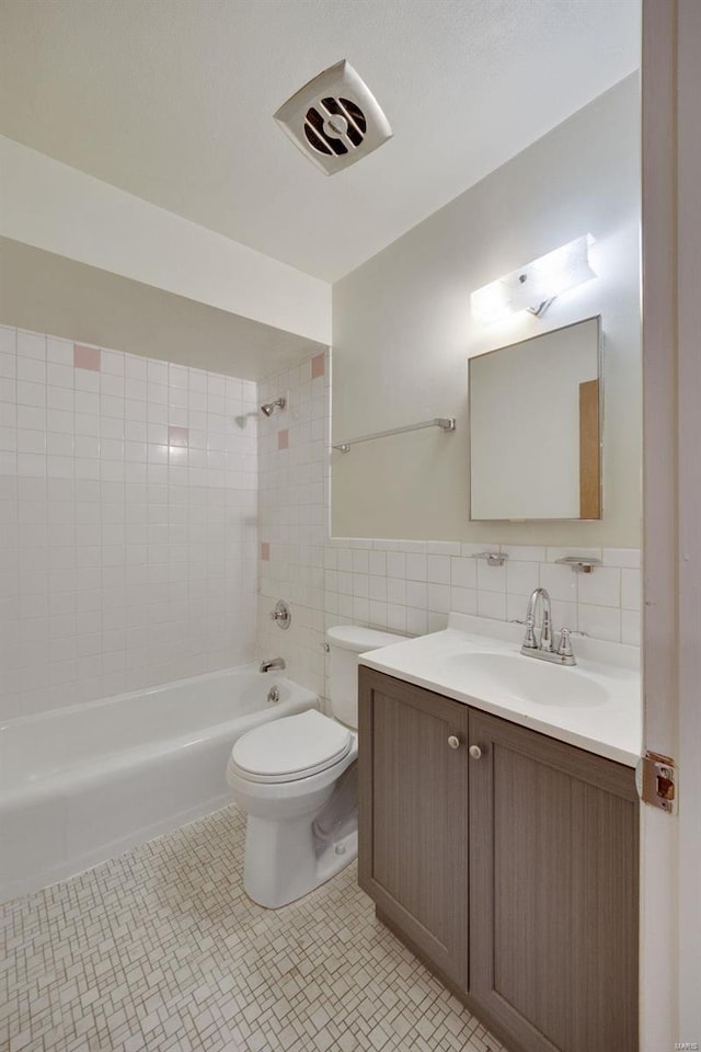 full bath featuring toilet, bathtub / shower combination, tile walls, vanity, and wainscoting