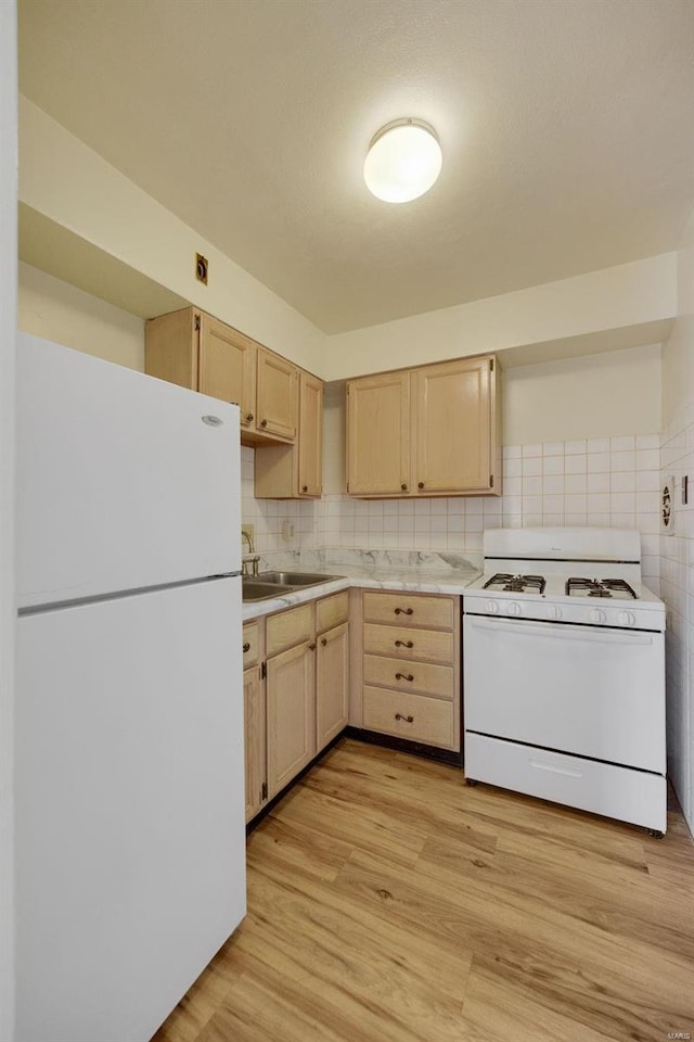 kitchen featuring white appliances, light brown cabinetry, light countertops, light wood-style flooring, and a sink