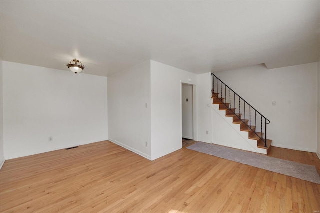 unfurnished living room featuring stairway, light wood finished floors, and baseboards