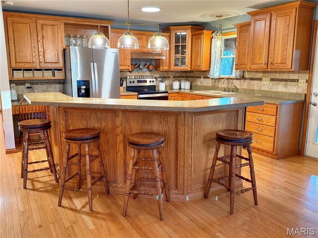 kitchen with stainless steel appliances, under cabinet range hood, light wood-style flooring, brown cabinets, and a sink