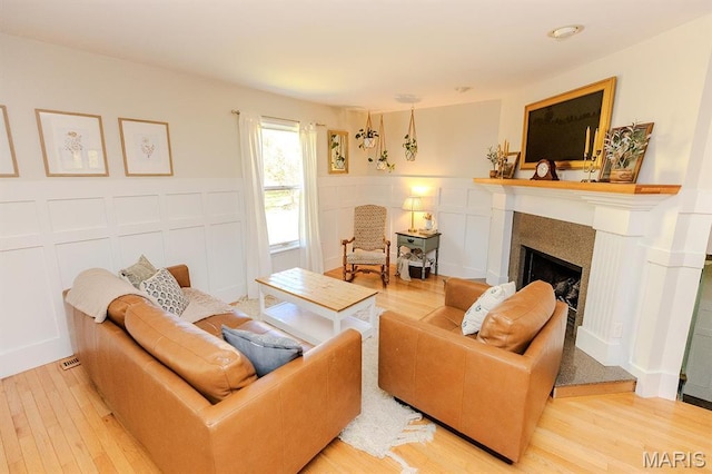 living room featuring a fireplace, a decorative wall, wood finished floors, and a wainscoted wall