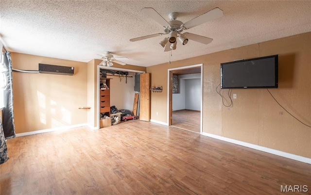 22125 Teak Ln, Saint Robert, MO 65584 - unfurnished living room with a textured ceiling, wood finished floors, ceiling fan, baseboards, and a wall unit AC