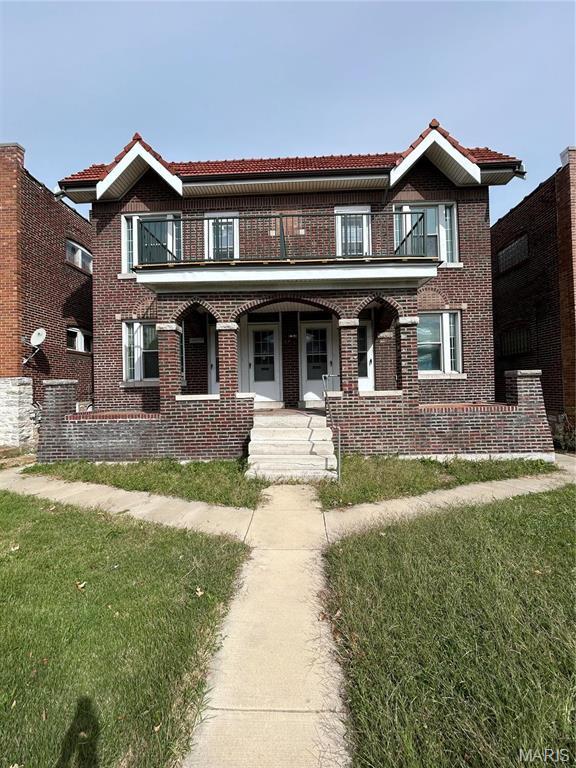 view of property with a balcony, covered porch, a tile roof, and brick siding