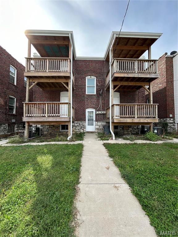 rear view of property featuring a balcony, a lawn, and brick siding