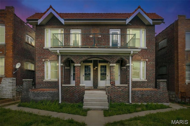 multi unit property featuring a balcony, a porch, brick siding, and a tiled roof