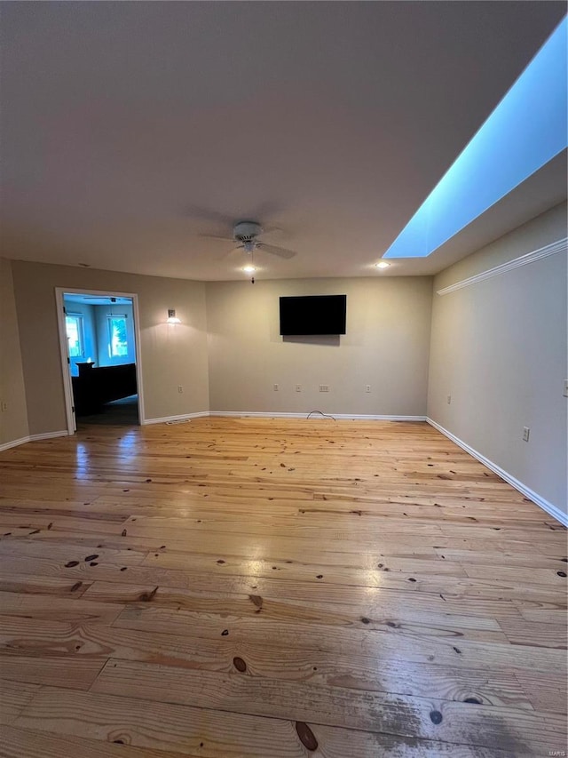 unfurnished living room with a ceiling fan, wood-type flooring, baseboards, and a skylight