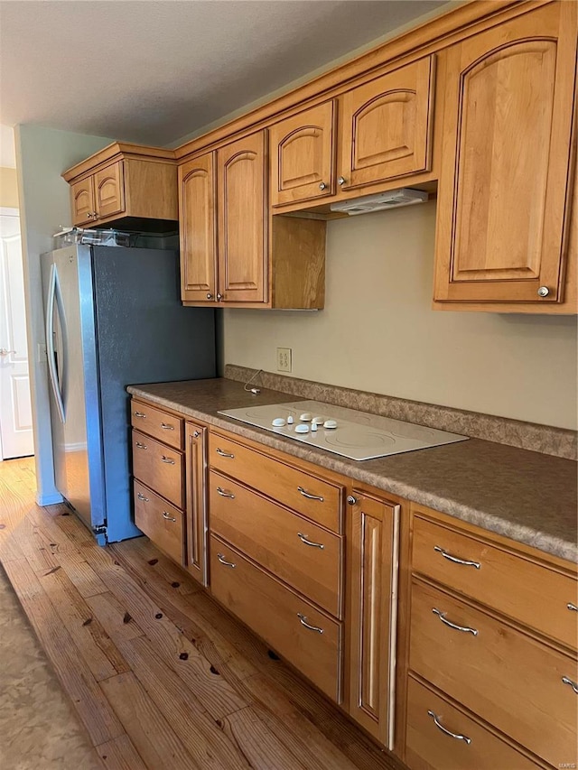 kitchen with white electric cooktop, dark wood-style flooring, freestanding refrigerator, and brown cabinets