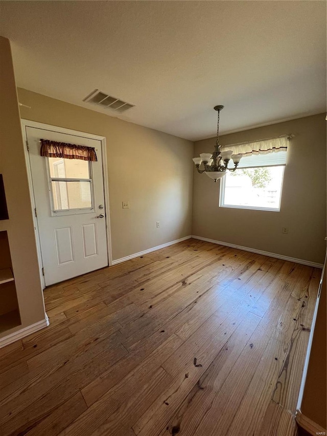 unfurnished dining area featuring a chandelier, hardwood / wood-style floors, and baseboards