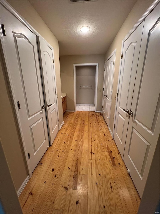 hall with baseboards, light wood-style flooring, and a textured ceiling