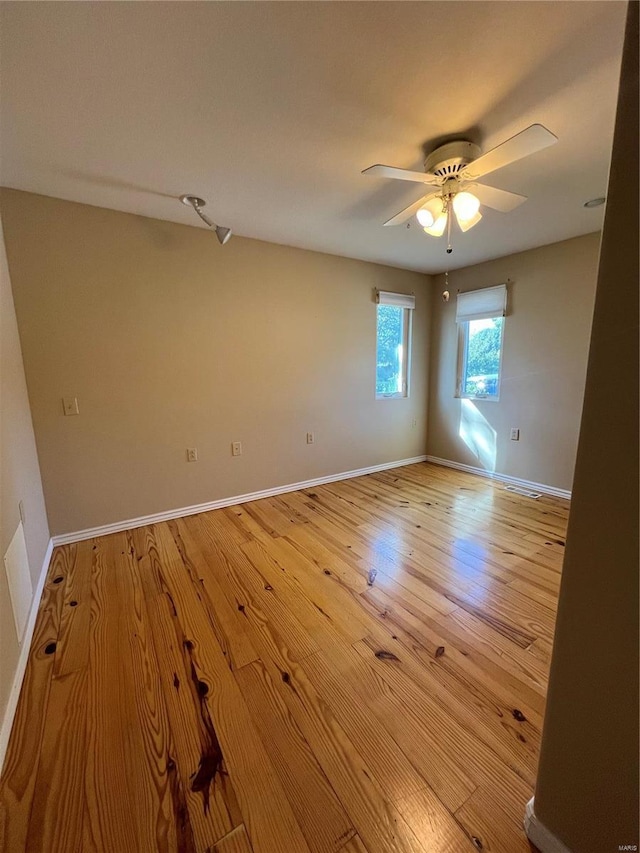spare room featuring light wood finished floors, a ceiling fan, and baseboards