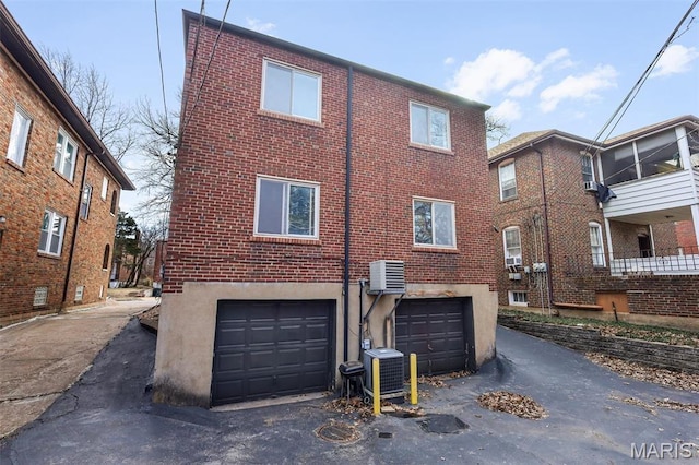 7273 Dartmouth Ave, Saint Louis, MO 63130 - rear view of house featuring a garage, central AC unit, brick siding, driveway, and stucco siding