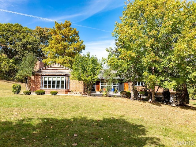 rear view of house with brick siding, a lawn, and a chimney