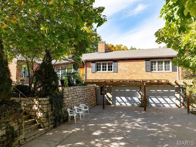 view of front of property featuring brick siding, an attached garage, a chimney, and concrete driveway