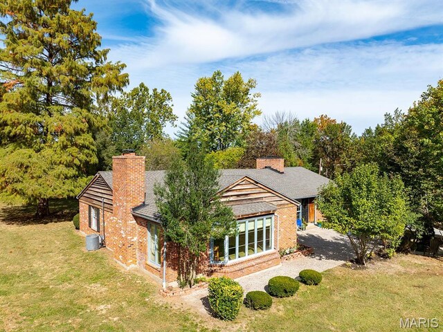 rear view of house with brick siding, a chimney, a yard, central AC unit, and a shingled roof