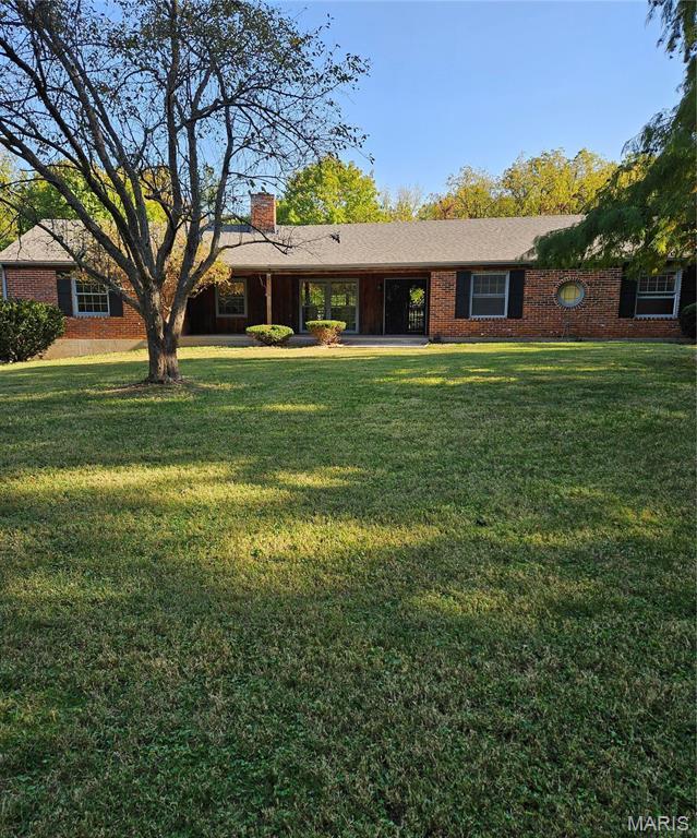 single story home with a chimney, a front lawn, and brick siding