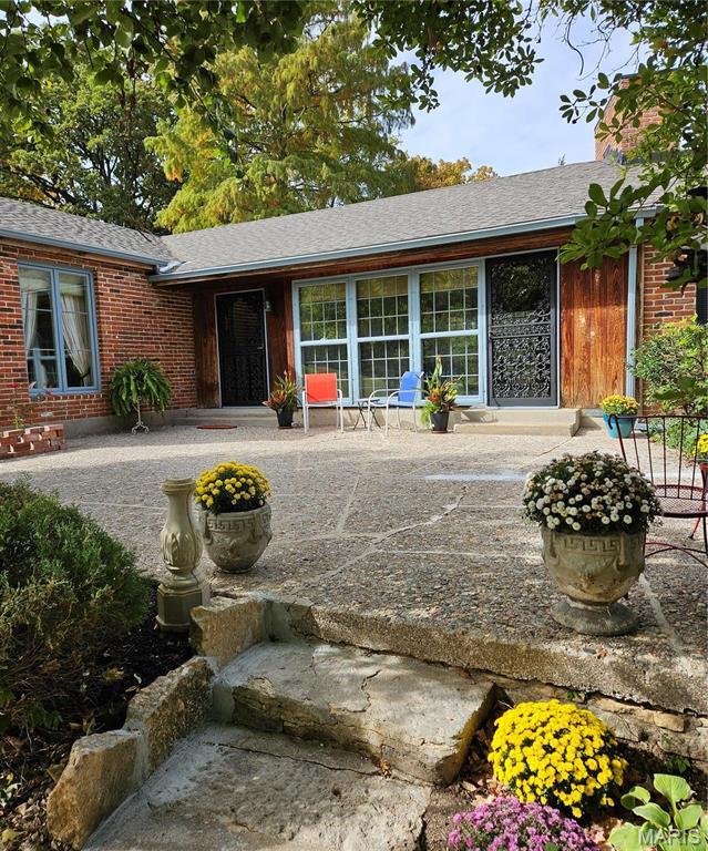 rear view of property with a chimney, brick siding, a shingled roof, and a patio
