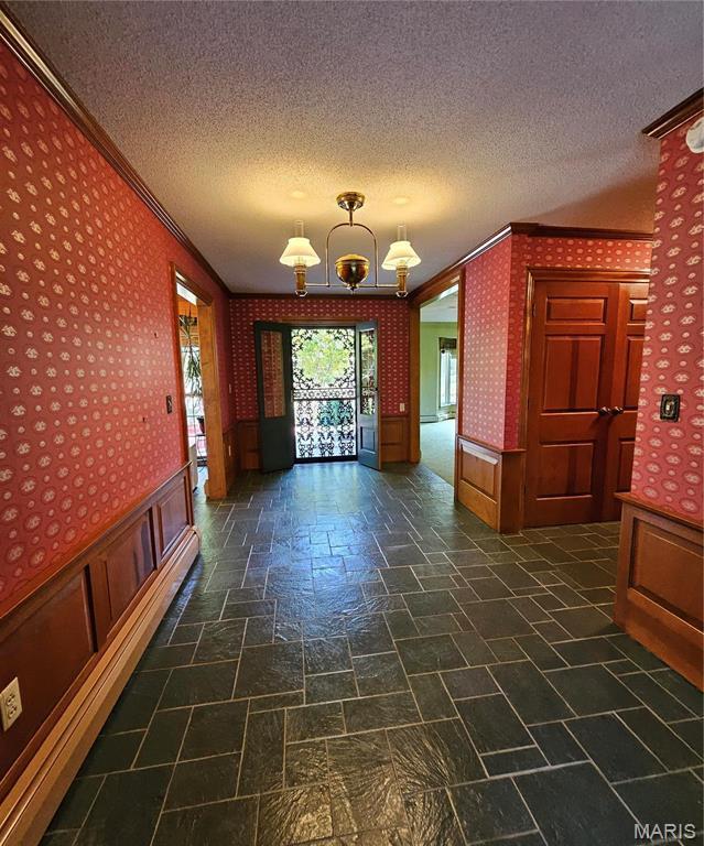 interior space featuring wallpapered walls, a chandelier, a textured ceiling, ornamental molding, and wainscoting
