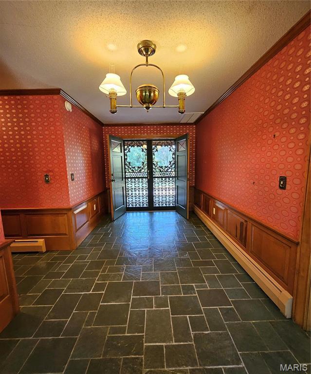 unfurnished room with ornamental molding, wallpapered walls, french doors, a wainscoted wall, and a baseboard heating unit