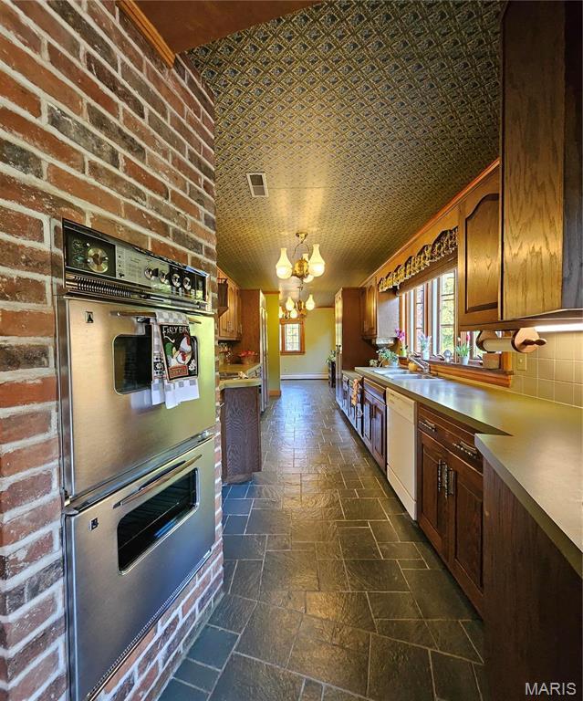 kitchen featuring white dishwasher, double oven, a chandelier, stone tile floors, and a sink